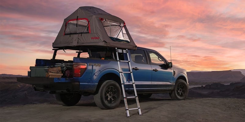 a 2025 ford f-150 parked with a tent set up pn the roof rails during sunset